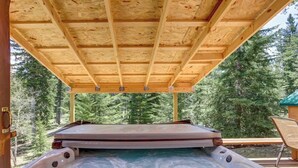 Un bain à remous installé sous une pergola en bois, avec vue sur une zone boisée.