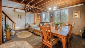 Un salon chaleureux avec un plafond en bois, une table à manger avec des chaises, un canapé et un escalier.