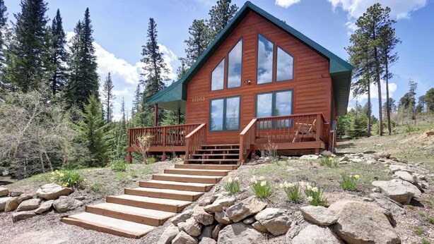 Une cabane en bois avec un escalier raide menant à une véranda dotée de sièges d’extérieur.
