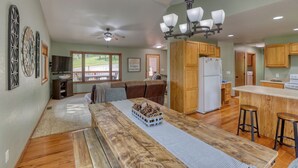 A spacious living area with a wooden dining table, a kitchen with wooden cabinets, and a ceiling fan. - Sunny Day Hideaway - Private! Firepit and Hot tub! (Sturgis)