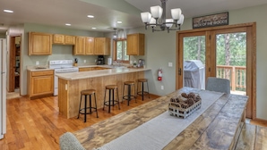 A spacious kitchen with wooden cabinets, a central island with stools, and a view of the outdoors through a sliding glass door. - Sunny Day Hideaway - Private! Firepit and Hot tub! (Sturgis)