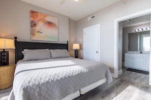 A bedroom with a large bed, two bedside tables, a wall-mounted lamp, and a door leading to a bathroom.