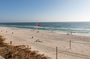 A beach with a red flag, sandy shore, and ocean waves.