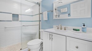 A bathroom with a glass shower enclosure, a white toilet, a sink with a mirror above, and a blue wall.