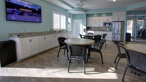 Una cocina amplia con armarios blancos, una isla grande con sillas, un televisor de pantalla plana y un ventilador de techo.