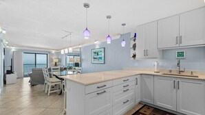 Een moderne keuken met witte kastjes, een centraal eiland, hanglampen en een eetgedeelte met uitzicht.