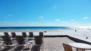 Un patio frente a la playa con sillas y mesas de metal, con vista al océano.
