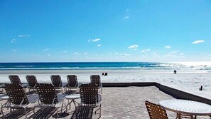 Un patio frente a la playa con sillas y mesas de metal, con vista al océano.