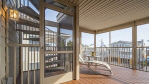 Une terrasse en bois avec une porte vitrée donnant sur un balcon, une petite table et un fauteuil rembourré.