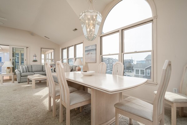 A spacious living room with a large dining table, comfortable seating, and large windows offering a view of the city.