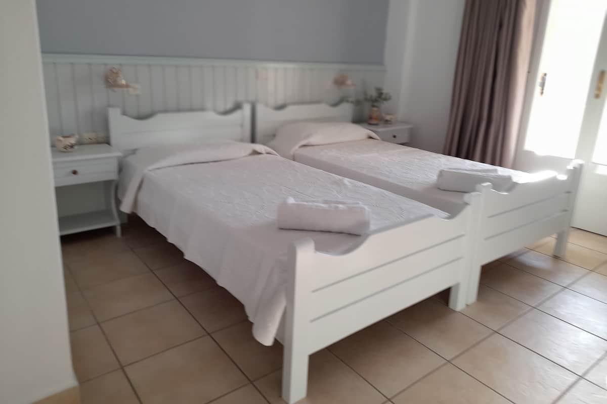 A double bed with a white headboard and footboard, a bedside table with a lamp, and a window with curtains.