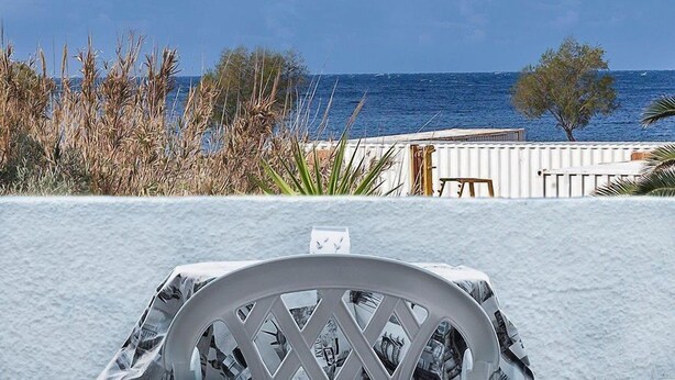 A white chair with a patterned cover, a white fence, and a view of the sea. - Elia (Patmos)