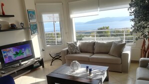 Ein Wohnzimmer mit Fernseher, Sofa, Couchtisch und einem Balkon mit Blick.