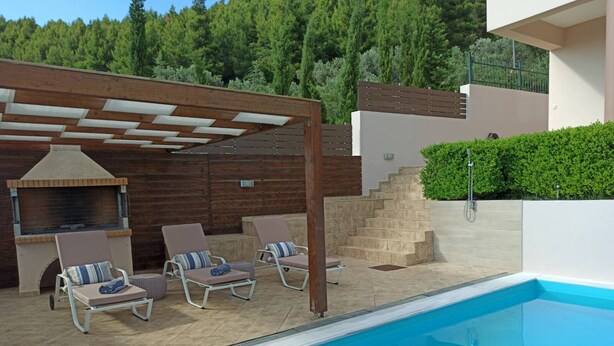 Ein Poolbereich mit Liegestühlen, einem Grill und einer Treppe zu einer überdachten Terrasse.