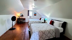 Una habitación pequeña y bien iluminada con dos camas, un escritorio, una silla y una lámpara.