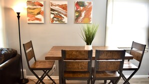 Un comedor con una mesa de madera y cuatro sillas, una planta en maceta y arte abstracto en la pared.