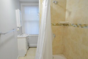 Un baño con ducha, lavamanos y espejo.