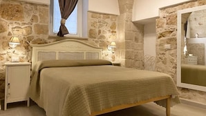 A bedroom with a stone wall, a bed with a wooden headboard, two bedside tables with lamps, and a window with a curtain. - moon (Monopoli)