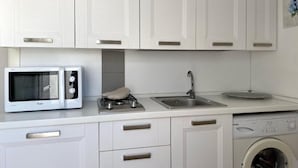 A modern kitchen with white cabinetry, a built-in microwave, a stove, a sink, and a washing machine. - moon (Monopoli)