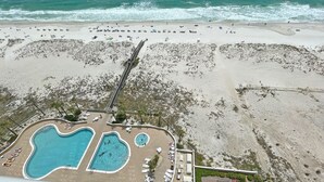 Ett flygbildsfoto av ett strandhotell med flera pooler, en lång brygga och en sandstrand.