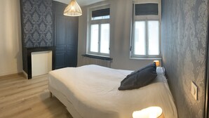 A bedroom with a bed, a radiator, a window, and a wall with a patterned wallpaper.