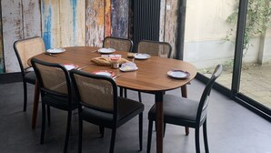 A dining area with a wooden table and chairs, a rustic wall, and a view through a glass door.