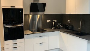 A modern kitchen with white cabinets, a built-in oven, a stainless steel range hood, a black countertop, and a black sink.