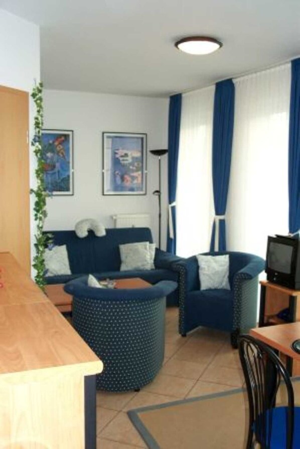 Een knus woongedeelte met een bank, fauteuils, een tafeltje en een televisie.