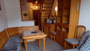 Ein gemütlicher Raum mit Holztisch, Bänken, einer Couch und einer Küchenzeile mit Holzschränken und Geräten.