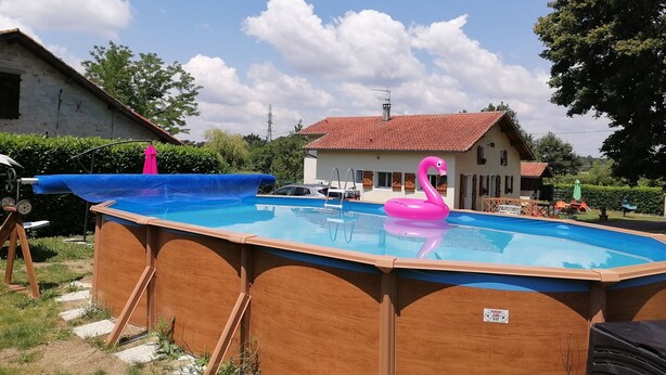 An above-ground swimming pool with a wooden deck, a pink flamingo float, and a house in the background. - Barn converted into gîte for 4/5 people (audon)