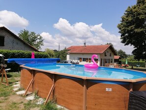 An above-ground swimming pool with a wooden deck, a pink flamingo float, and a house in the background.