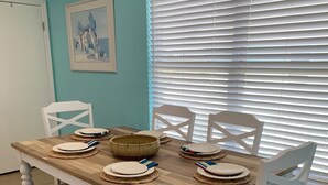 Une table à manger avec des chaises blanches, un plateau en bois et des sets de table en fibres tressées.