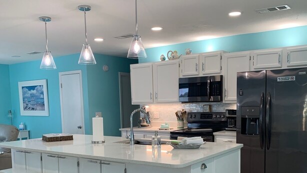 Une cuisine moderne dotée d’un îlot central, de tabourets de bar blancs, d’appareils électroménagers en acier inoxydable et de murs de couleur turquoise.