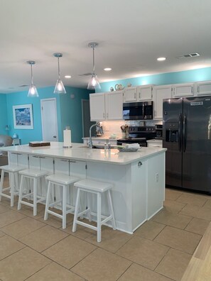 Une cuisine moderne dotée d’un îlot central, de tabourets de bar blancs, d’appareils électroménagers en acier inoxydable et de murs de couleur turquoise.