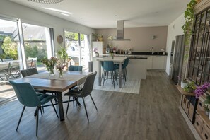 Une cuisine moderne dotée d’un îlot central, d’un coin repas avec des chaises et de grandes fenêtres.
