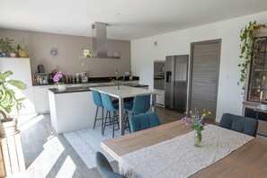 A modern kitchen with a central island, bar stools, a dining table with a rug, and a refrigerator.