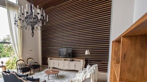 A modern living room with a wooden slatted wall, a chandelier, a television, and a sofa. - Pousada Recanto das Araras (Tiradentes)