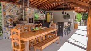 A wooden dining table with benches, a kitchen area with a TV, and a bar with stools. - Pousada Recanto das Araras (Tiradentes)