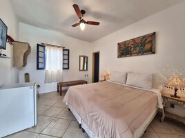 A bedroom with a bed, bedside lamps, a ceiling fan, a mirror, and a painting.