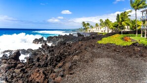 A coastal hotel with a rocky shoreline, palm trees, and ocean views. - KKSR#2304 DIRECT OCEANFRONT, INCREDIBLE TOP FLOOR CORNER UNIT, HUGE LANAI! (Kailua Kona)