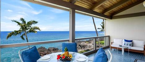 A dining area with a table set for two, overlooking the ocean with a view of the beach and palm trees.
