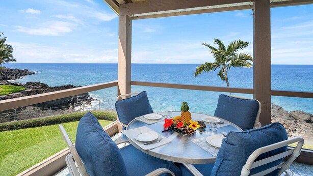 A table set for two with a view of the ocean and a palm tree. - KKSR#2304 DIRECT OCEANFRONT, INCREDIBLE TOP FLOOR CORNER UNIT, HUGE LANAI! (Kailua Kona)