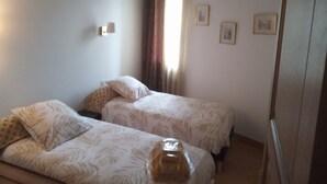 Ein Zimmer mit zwei Betten, einem Fenster mit Vorhängen und einer Wandleuchte.