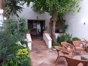 Un espace extérieur aménagé en terrasse, avec des meubles en osier, des plantes en pot et un escalier menant à un espace intérieur.