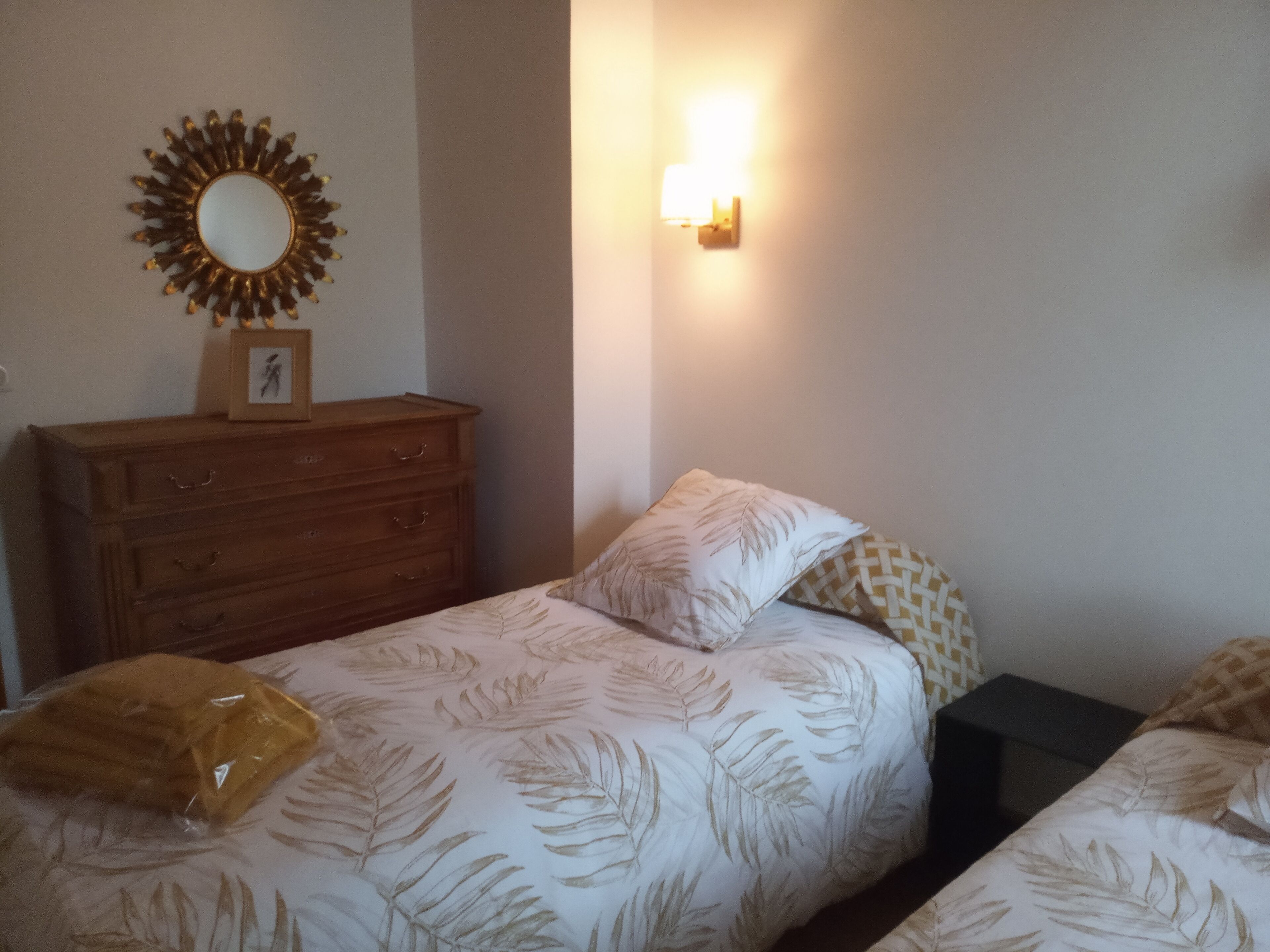 Un dormitorio con dos camas individuales, un aparador de madera, una lámpara en la pared y un espejo.