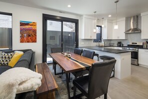 A modern kitchen with white cabinets, a central island, and a dining area with a wooden table and chairs. - Downtown Moab | Steps from Bike Path & Restaurants (Moab)