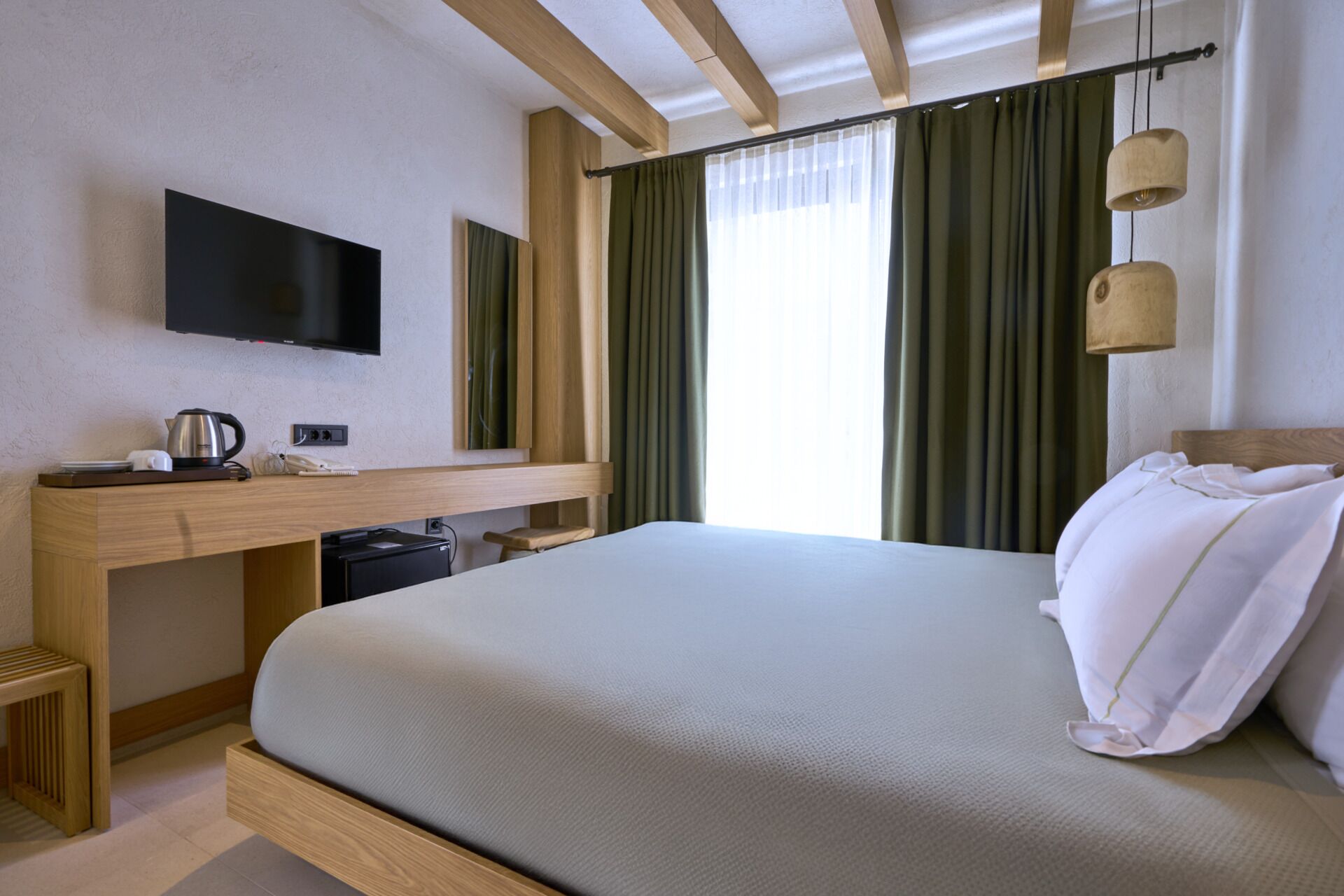 Habitación de hotel con cama, escritorio con televisor de pantalla plana, cafetera y un taburete pequeño.