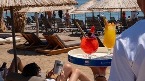 A beach with sun loungers and umbrellas, a drink on a tray, and people relaxing. - Club Kavala Beach Hotel Assos (Ayvacik)