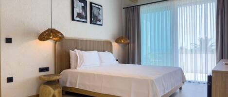 A modern hotel room with a large bed, wooden beams, a round side table, and a large window with curtains.