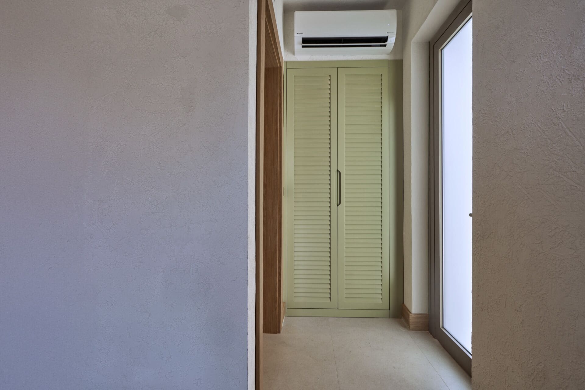 A narrow hallway with a green door and a window on the right.